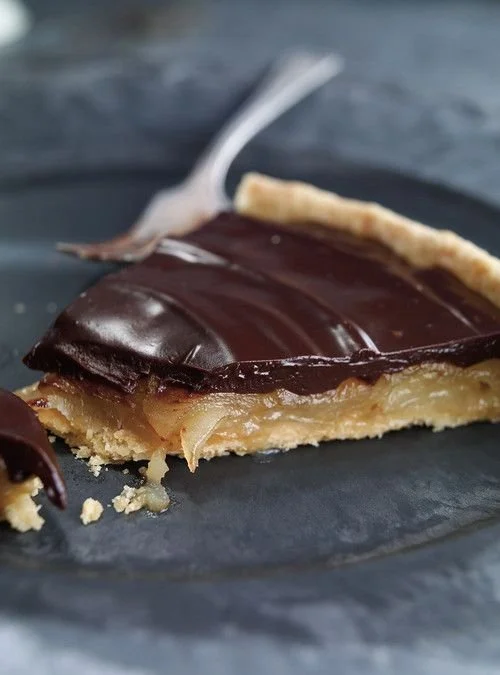 Tarte aux poires caramélisées et chocolat sur une assiette, garnie de crème.